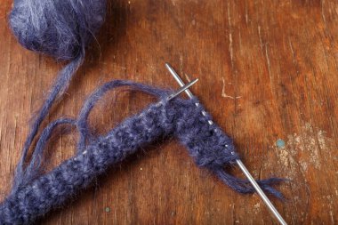 Eski ahşap arka planda örgü iğneleri ve koyu mavi yün yumağı. Örgü örmeye başlıyorum, üst görünüm.