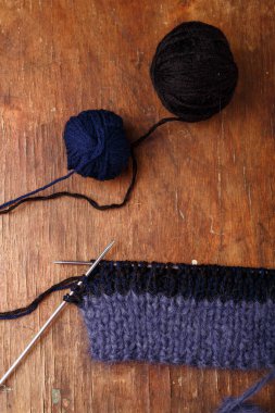 Örgü iğneleri, koyu mavi saç telleri ve eski ahşap masa arkasında siyah akrilik iplik topları. Örgü örmeye başlıyorum..