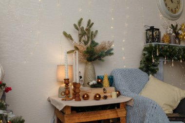 İzmail, Ukrayna. Aralık 2023. Güzel Noel süslemeleri, fener, ampul ve mumlar, köknar dallı vazo. Ekose ve minderler. Duvardaki saat