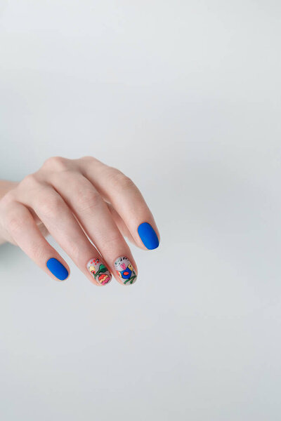 Nail art with blue gel varnish and floral design on woman's hand. Manicure salon service. White background, copy space. Vertical shot.