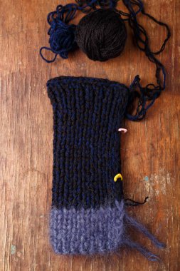 Eski ahşap arka planda koyu mavi saç örgüsü ve akrilik iplik topları. İğneli örgü bir elbisenin parçası.