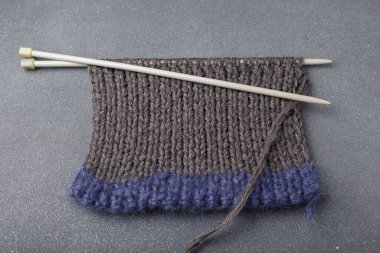 Gri arkaplanda örgü örgüsü ve akrilik iplik kumaşı parçaları olan örgü iğneleri..