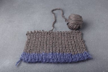 Gri arka planda örülmüş saç örgüsü ve akrilik giysinin bir parçası. Örgü yumağı..