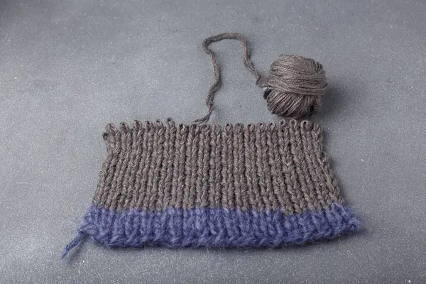 Gri arka planda örülmüş saç örgüsü ve akrilik giysinin bir parçası. Örgü yumağı..