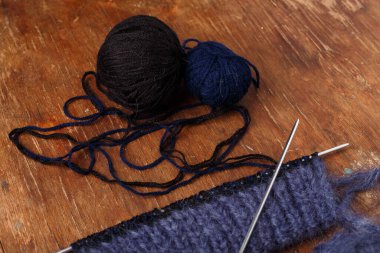 Örgü iğneleri, koyu mavi saç telleri ve eski ahşap masa arkasında siyah akrilik iplik topları. Örgü örmeye başlıyorum..