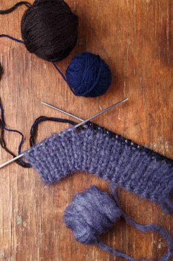 Örgü iğneleri, koyu mavi saç telleri ve eski ahşap masa arkasında siyah akrilik iplik topları. Örgü örmeye başlıyorum..