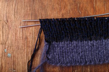 Örgü iğneleri, koyu mavi saç teli ve eski ahşap masa arkasında siyah akrilik iplik şeritleri. Örgü örmeye başlıyorum..
