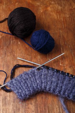 Örgü iğneleri, koyu mavi saç telleri ve eski ahşap masa arkasında siyah akrilik iplik topları. Örgü örmeye başlıyorum..