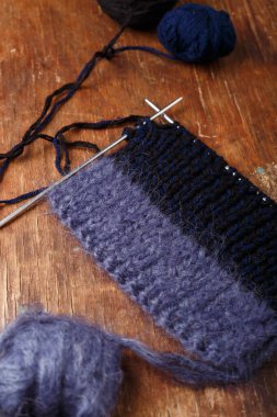 Örgü iğneleri, koyu mavi saç telleri ve eski ahşap masa arkasında siyah akrilik iplik topları. Örgü örmeye başlıyorum..