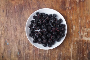 Kahverengi eski ahşap masa üzerinde beyaz tabakta taze böğürtlen, üst görüş, kopyalama alanı.