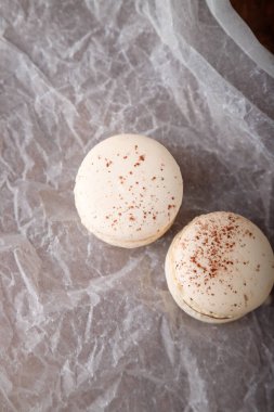 Çikolata dolgulu bej badem kurabiyeleri, kahve veya kapuçino aromalı kapuçino ve kağıt üzerinde kakao tozu, ahşap arka plan