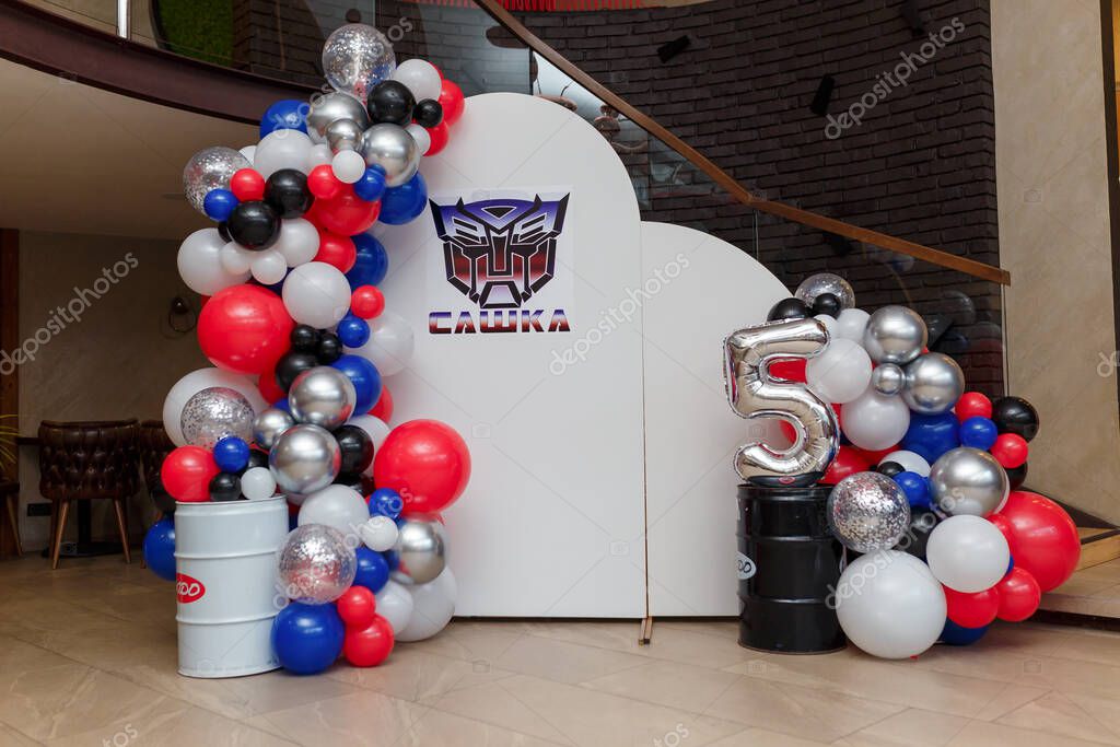 Izmail, Ukraine. July 2024. Multicolor balloons decoration for 5 years old boy birthday party. Photo zone with Transformers logo on white background.