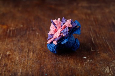 Pembe mor ve mavi desenli mum, eski ahşap masa arka planında doğal arı cilasından yapılmış bir çiçek şeklinde. Yakın çekim..