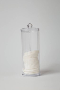 Yüz bakımı için yuvarlak pamuk süngerler, mendiller ya da peçeteler şeffaf kutuda tıbbi tedavi ya da güzellik prosedürleri, beyaz arka planda kapaklı yarı boş konteynır. Uzayı kopyala, dikey çekim