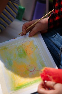 Yumuşak yağlı pastel tebeşirle resim yapan ya da çizen kadın eller beyaz kağıttaki sıcak renklerin arka planını oluşturur. Yumuşak odaklı yakın çekim.