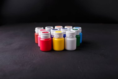 Küçük renkli akrilik ya da guaj boya kavanozlarını koyu arkaplanda bir kutuya koyarız. Sanat malzemeleri. Boşluğu kopyala.