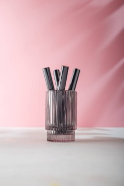 Göz, maskara tüplerinin şablonunu pembe arka planda camla kirpikliyor. Markasız, etiket ürünü reklamı yok. Boşluğu kopyala