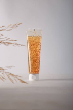 Beyaz üzerine kozmetik tüpü, ön planda bitki. Marka yok, etiket kutusu yok cilt temizleyici ya da ovalayıcı yok. Ürün reklam afişi. Boşluğu kopyala.