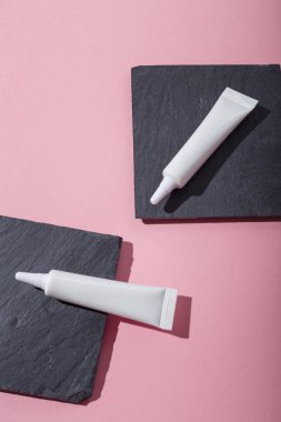 Beton tezgahların üzerinde iki beyaz, markasız kozmetik tüpü, pembe arka plan. Güzellik ürünü şablonu, reklam afişi. Uzayı kopyala Flay lay lay, üst görünüm.