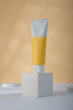 Sarı Kozmetik tüp modeli beton kübün üzerinde, sarı arka plan. Markasız güzellik kutusu, etiket şablonu yok. Ürün reklam afişi, kopyalama alanı