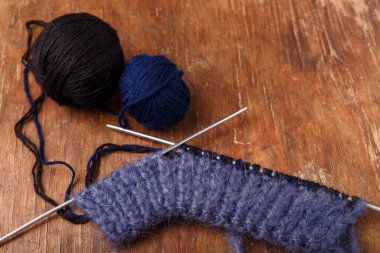 Örgü iğneleri, koyu mavi saç telleri ve eski ahşap masa arkasında siyah akrilik iplik topları. Örgü örmeye başlıyorum..