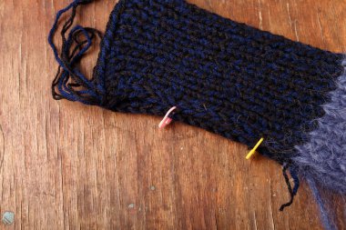 Eski ahşap arka planda koyu mavi saç teli ve akrilik iplik örüyorum. İğneli örgü bir elbisenin parçası.