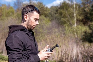 A man a drone pilot with a control panel in his hands controls a quadcopter in the field outdoor.