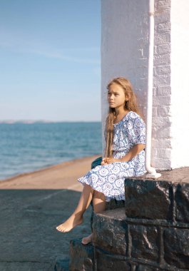 Deniz kenarında düşünceli bir şekilde duran sevimli, yalnız, küçük bir kızın portresi. Rüyalar, endişeler, endişeler