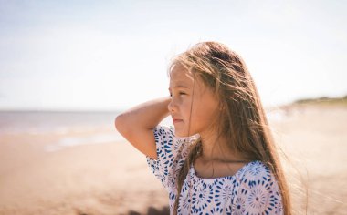 Deniz kenarında düşünceli bir şekilde duran sevimli, yalnız, küçük bir kızın portresi. Rüyalar, endişeler, endişeler