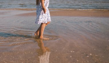 Kızın bacakları kapalı. Kumda ve deniz kıyısında yalınayak. Bir kızın ayakları bir çocuğun deniz kıyısında yürümesi. Yaşam biçimi