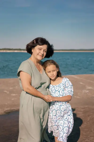 Portrait of Grandmother  with her little granddaughter spent weekend and walking on sea coast at sunny summer.