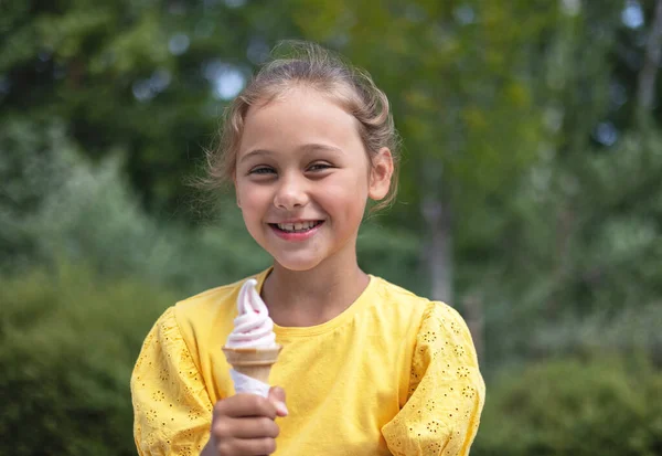 Cute laughing child little girl eats ice cream on a hot day. Ice cream in a waffle cone. A happy and contented child at summer.