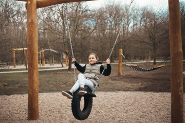 Oyun parkındaki bir kız salıncakta sallanırken eğleniyor.