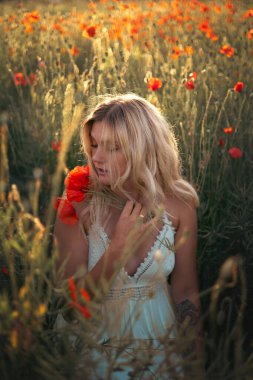 Gün batımında haşhaş tarlasında beyaz elbiseli güzel sarışın kadın. Kadın ve doğa