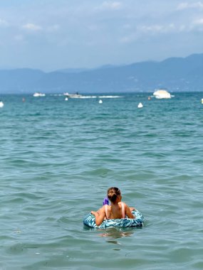 Kız şişme bir yüzükle gölde yüzüyor. Garda Gölü 'nde tatiller