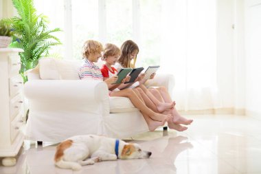 Çocuklar beyaz kanepede oynar ve televizyon izler. Evdeki çocuklar. Sunny aile odası, içinde küçük bir çocuk olan aile evi. Kız ve erkek kanepede oturmuş bilgisayar oyunu oynuyorlar. Modern evdeki oturma odası..