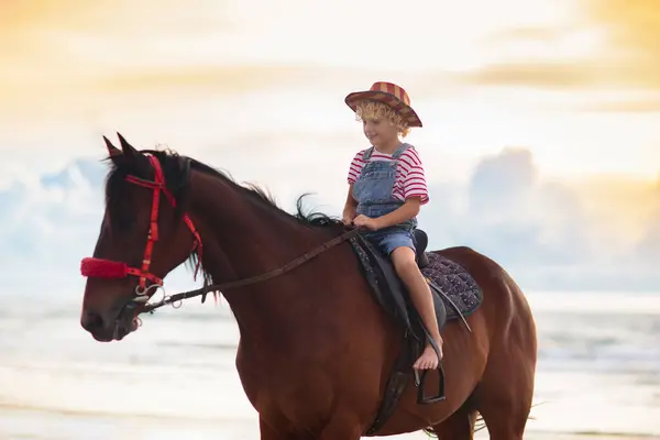 孩子们骑马在海滩上 孩子们骑马 在加利福尼亚或佛罗里达海岸度暑假时 戴着牛仔帽 头戴美国国旗的金发可爱孩子 美国男孩骑在他的小马在农场 儿童和动物 — 图库照片