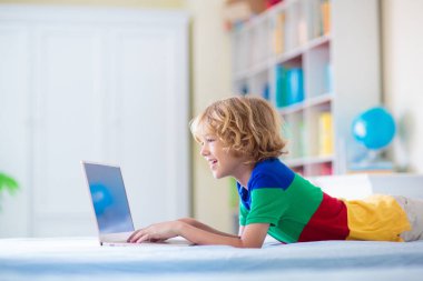 Bilgisayarda ödev yapan bir çocuk. Çevrimiçi sınıf. Evde eğitim ve uzaktan eğitim. Küçük okul çocuğu monitörde okuyor. Çocuklar video oyunu oynar. Oyun ve ekran zaman denetimi.