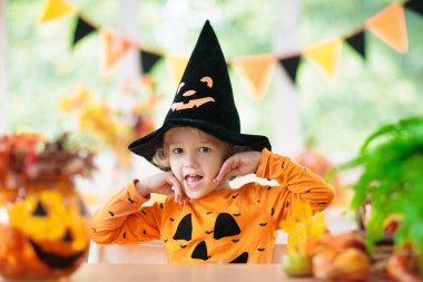 Cadılar Bayramı kostümlü çocuk. Çocuklar şeker mi şaka mı? Balkabağı fenerli küçük çocuk. Cadı şapkalı bebek. Sonbahar tatili dekorasyonu. Dökülen yapraklar ve kabaklarla ev şenliği. 
