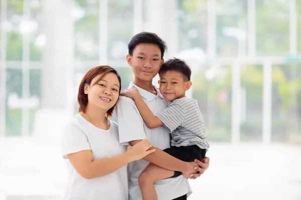 Mom and kids in restaurant. Asian family eating out. Beautiful young mother and two boys in white sunny room.