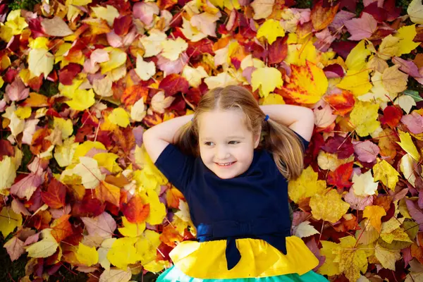 Çocuklar sonbahar parkta oynamak. Sarı ve kırmızı yaprakları atan çocuklar. Meşe ve akçaağaç yaprağı ile küçük kız. Sonbaharda yapraklar. Güz aile açık eğlence. Yürümeye başlayan çocuk veya okul öncesi çocuk Güz.