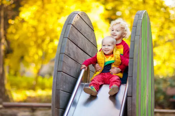 子供たちの遊び場でお子様は秋の公園で遊ぶ スライドとスイングの晴れた秋の日に上の子 保育園か幼稚園の庭 若い子供のための保育園 赤ちゃんプレイ グラウンド 秋の屋外の楽しみ ロイヤリティフリーのストック写真