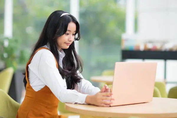ラップトップを持つ美しいアジアのティーンエイジャーの少女 レストランでコンピュータで働く長髪の若い女性 宿題をする学生 フリーランスのオンラインワーク ブログを書く ブログ投稿 ストックフォト
