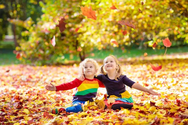 秋の公園で子供たちが遊ぶ 子供たちが投げて黄色のカエデの葉 男の子と女の子は ジャンプ オークの葉で実行します 秋の紅葉 秋の家族の屋外の楽しみ 幼児の子供と幼児子供は秋に ストック写真