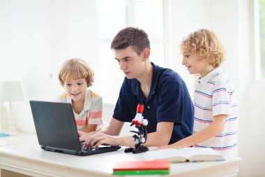 Mikroskoplu okul çocukları. Fen dersi. Dizüstü bilgisayarla biyoloji ya da kimya deneyi yapan çocuklar. Çevrimiçi öğrenme. İlkokul çocuğuna uzaktan eğitim. Çocuk konuya bakıyor..