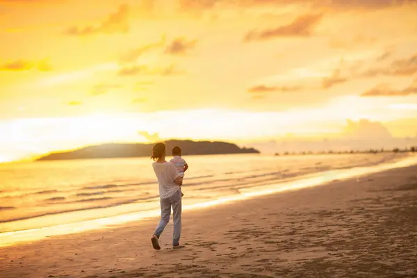日没のトロピカルビーチで母と赤ちゃん 歩き回って海で遊んでいる幼児のアジア人女性 若いママと小さな男の子は海岸を歩いています 子供たちと旅をする 幼い子供との休暇 — ストック写真