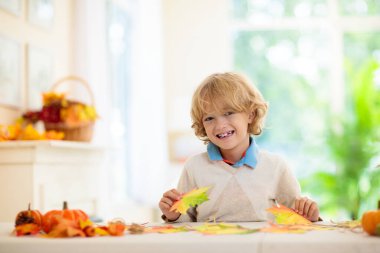 Sonbahar ev dekorasyonu. Renkli akçaağaç yapraklı aile dekorasyonu evi. Beyaz oturma odasında Şükran Günü ya da Cadılar Bayramı kutlaması. Düşen yapraklı çocuk. Yapraklı yaratıcı fikirler üretir..