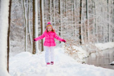 Çocuk kışın karla oynuyor. Noel 'de kış parkında kar taneleri yakalayan renkli ceketli ve örgü şapkalı küçük bir kız. Çocuklar karlı ormanda oynayıp zıplıyorlar. Çocuklar kar tanelerini yakalar