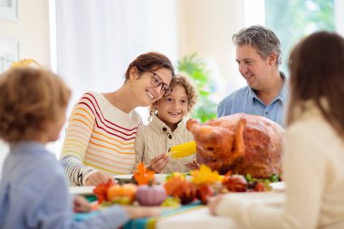 Şükran Günü yemeğinde aile yemeği. Ebeveynler ve çocuklar kızarmış hindi ve sebzeleri severler. Anne, baba ve çocuklar birlikte şenlikli yemek yiyorlar. Sonbahar tatili ev dekorasyonu ve masa düzenleme.