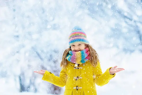 Child in knitted hat playing in snow on Christmas vacation. Winter outdoor fun. Knitting and outerwear for family. Kids play in snowy park. Little girl in knit scarf and mittens catching snowflakes.